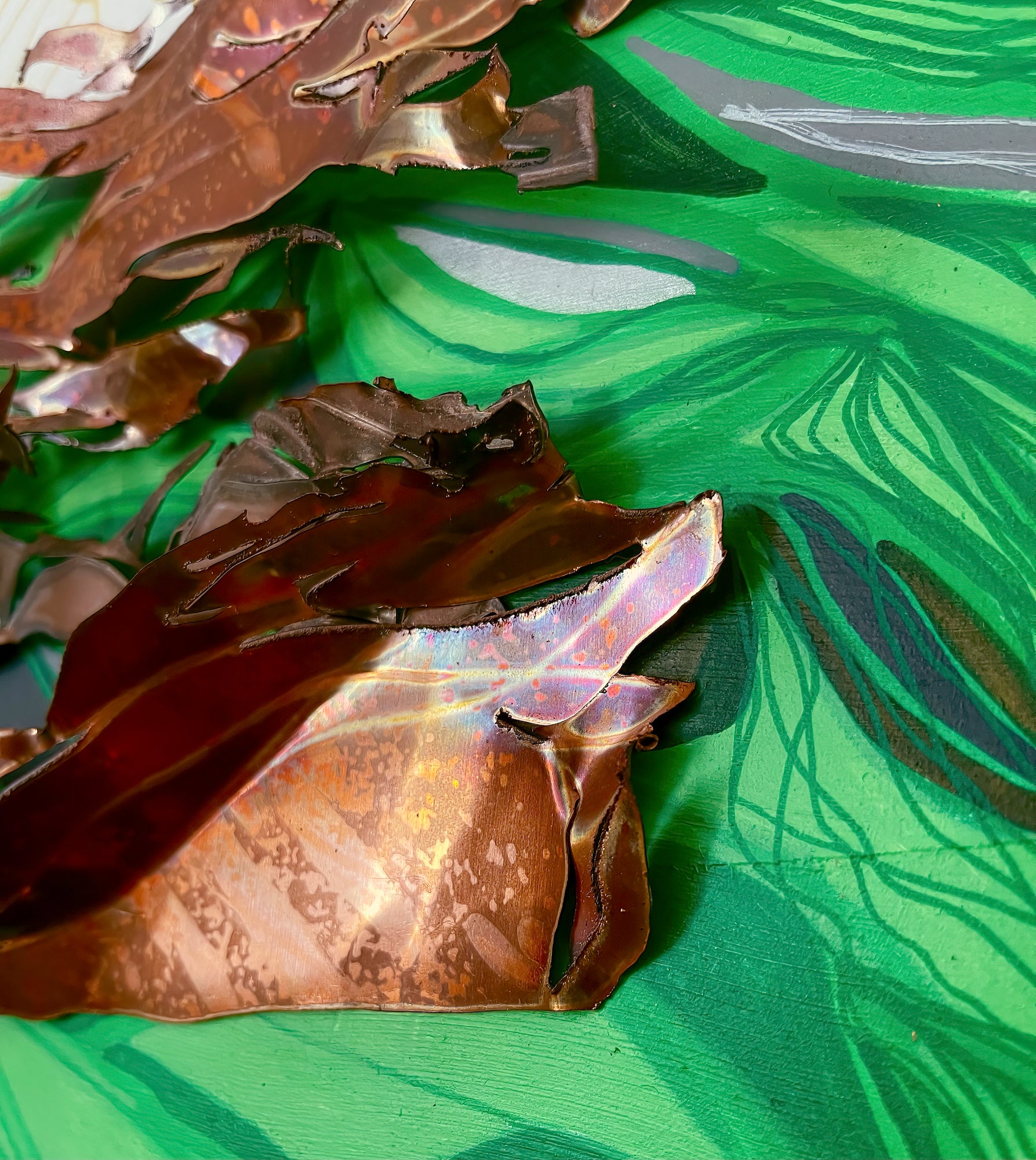 This close up image shows the 3 dimensional aspect of the copper sections which are cut and bent in a tangled form. The underlaying color is a mix of green tones. 