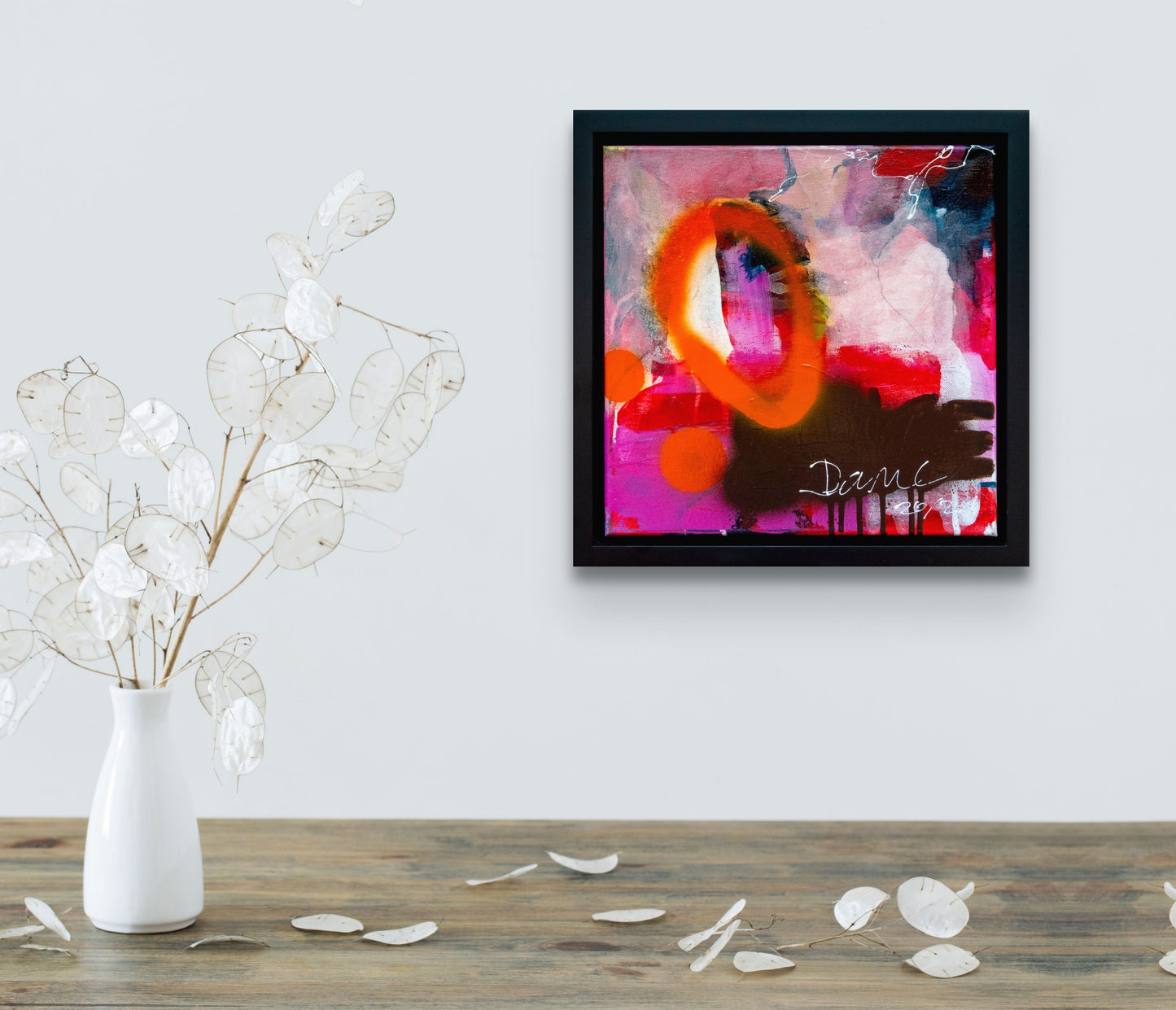 Colorful abstract painting using acrylic paint titled 'Dance' by artist Steffi Möllers; measures 12"x12" and 14"x14" with black frame; in situ on wall with vase filled with paper-like leaves