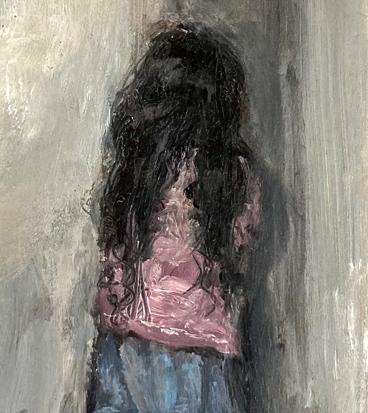 A zoomed image of the small girl standing in the corner wearing a pink shirt and blue skirt. Her hair is long and black, the walls are gray.