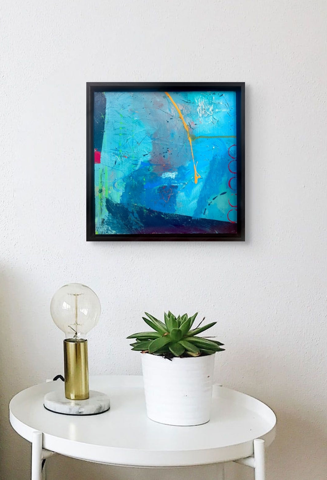 The third in the Blue Series is hanging on a white wall over the circular table with a lamp and plant.