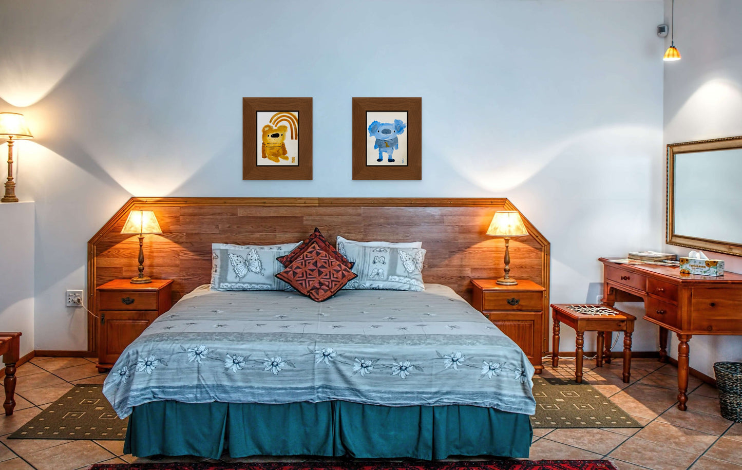 This image shows both of April Bedard paintings hanging over a bed with a teal bedspread and a wooden headboard. The paintings have been framed in matching frames and work well as a set. 