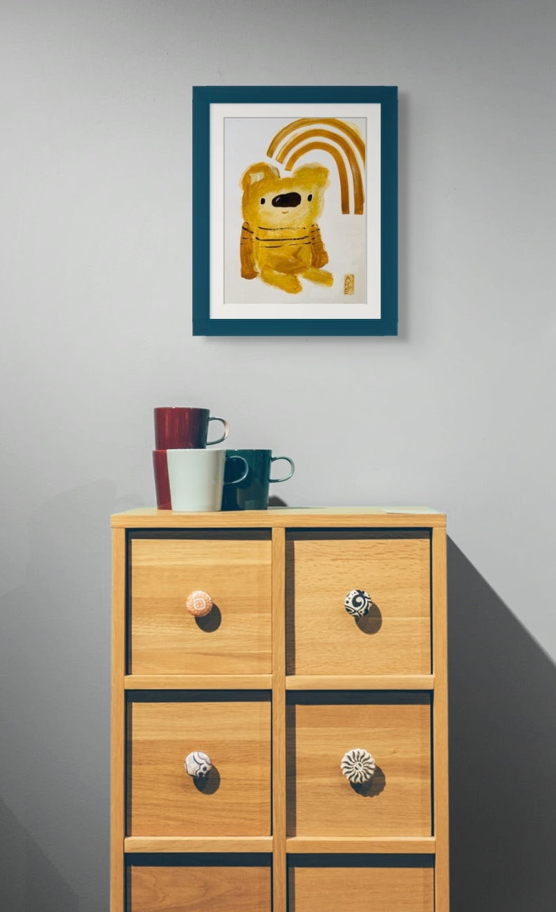 Here Brown Bear and Rainbow is framed with a white mat and dark green frame. It is hanging over a small dresser which has four coffee cups of different colors stacked on its top. 