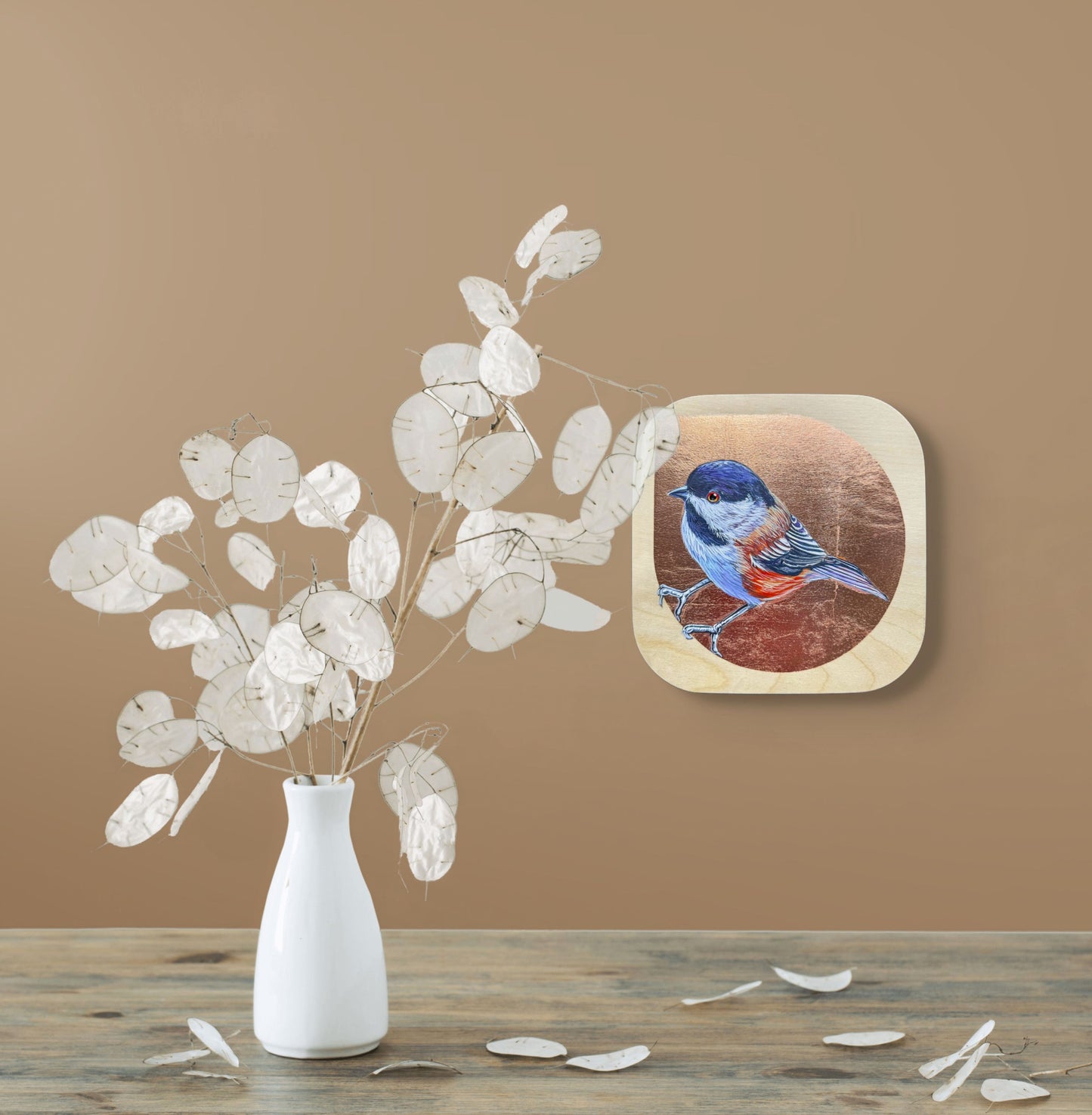 Colorful Chickadee against a copper leaf background; painted on a birch panel; 8"x8"; shown in situ on beige wall with white vase and leaves; artist Marie Lavallee