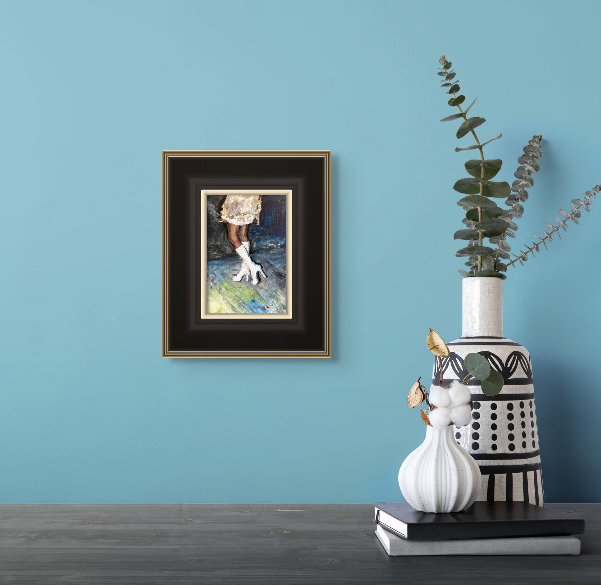 In situ photo of Fantasia framed in a black frame over a table adorned with a few books and two vases.