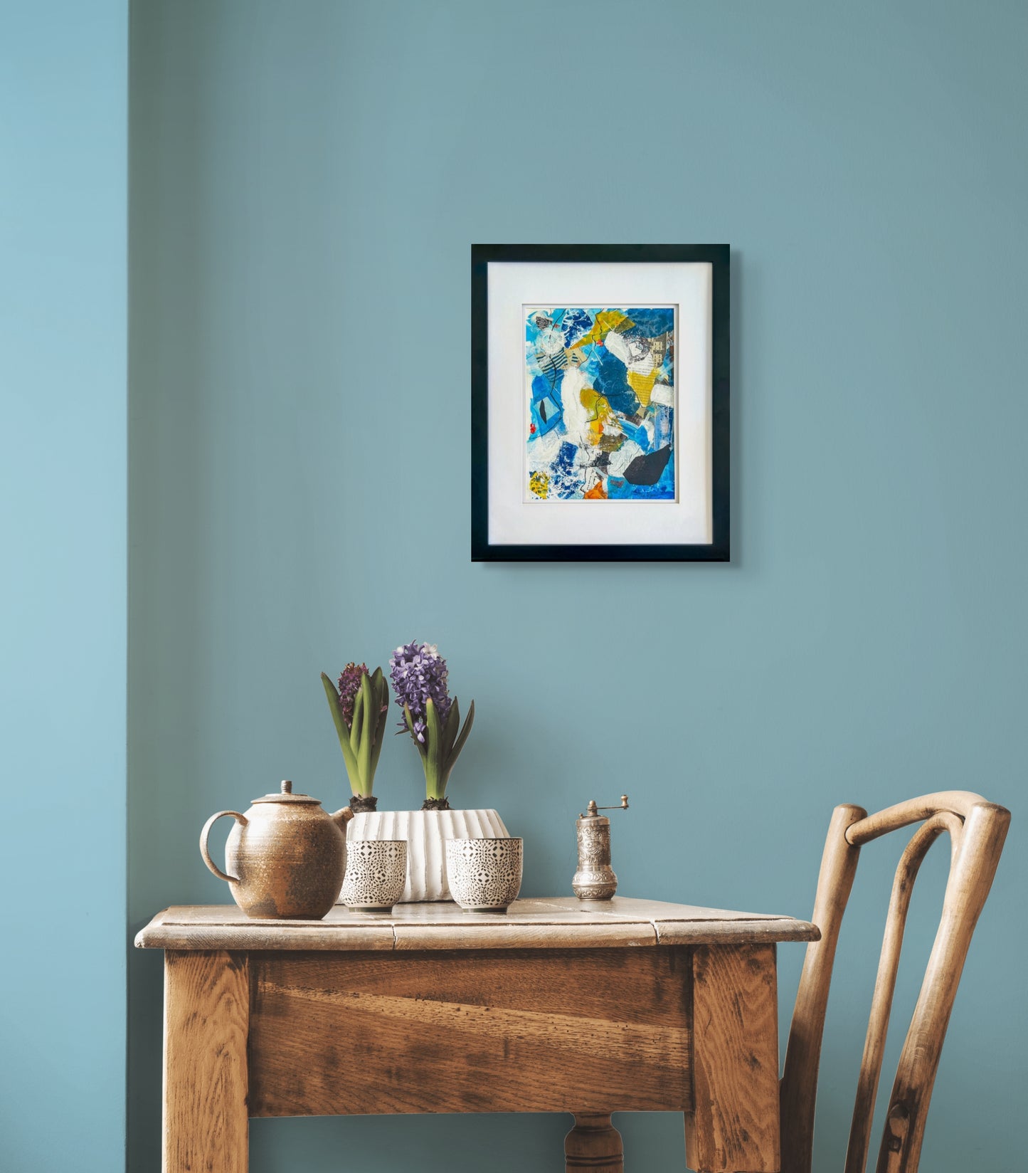 Abstract mixed media piece in hues of blue, yellow, white and black. Image includes newsprint and collage papers; shown in situ with white mat and narrow black frame; artist Bob Hogue