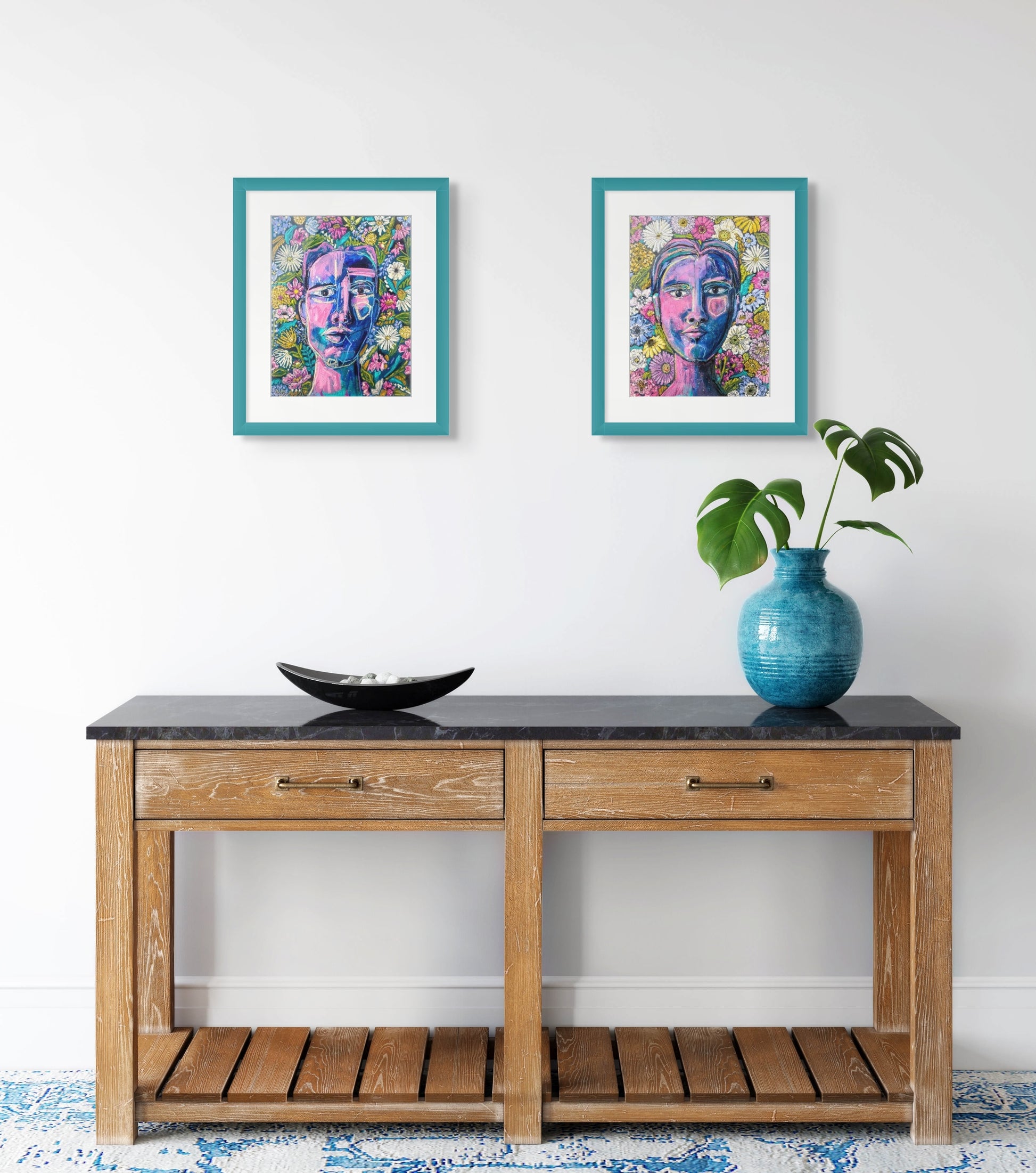 In situ image of both of Rachel Bunteman's portraits hanging as a pair above a hall table adorn with a blue vase and plant. The portraits are framed in a teal wooden frame with a white mat.