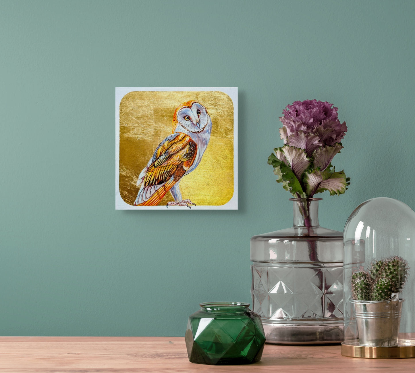 In situ view of Head Tilt hanging on a light green wall over a table adorned with vases and a candle. 