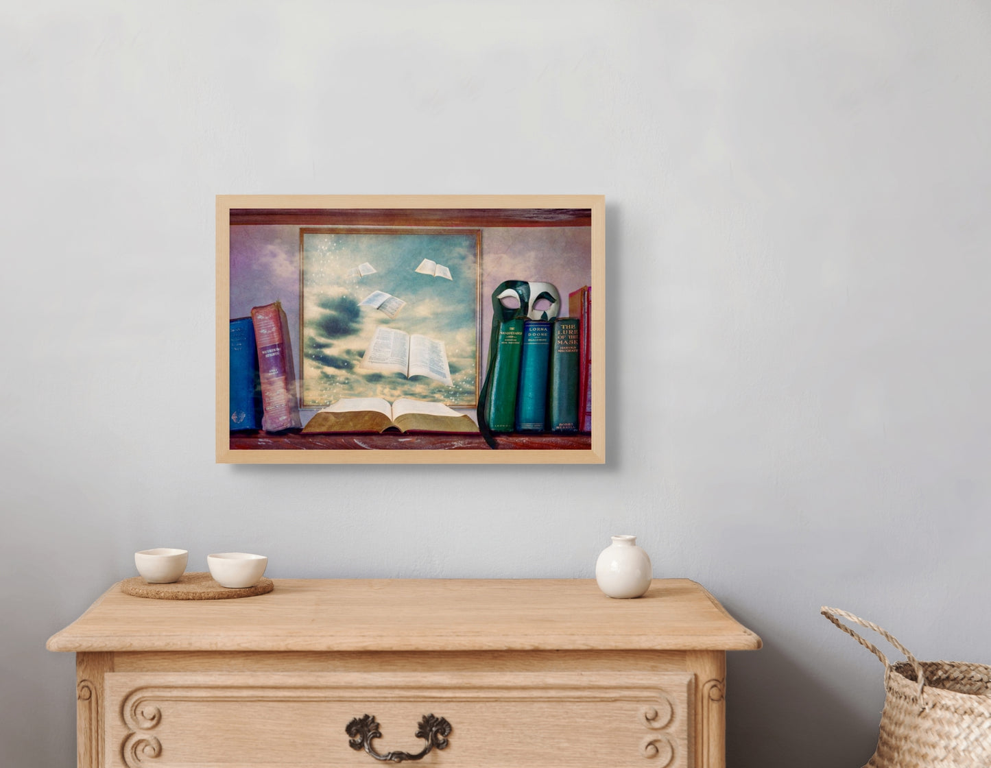 Lost Pages hangs over a small dresser, framed in a ash wooden frame which matches the dresser.  A small vase and two small bowls sit on the dresser.