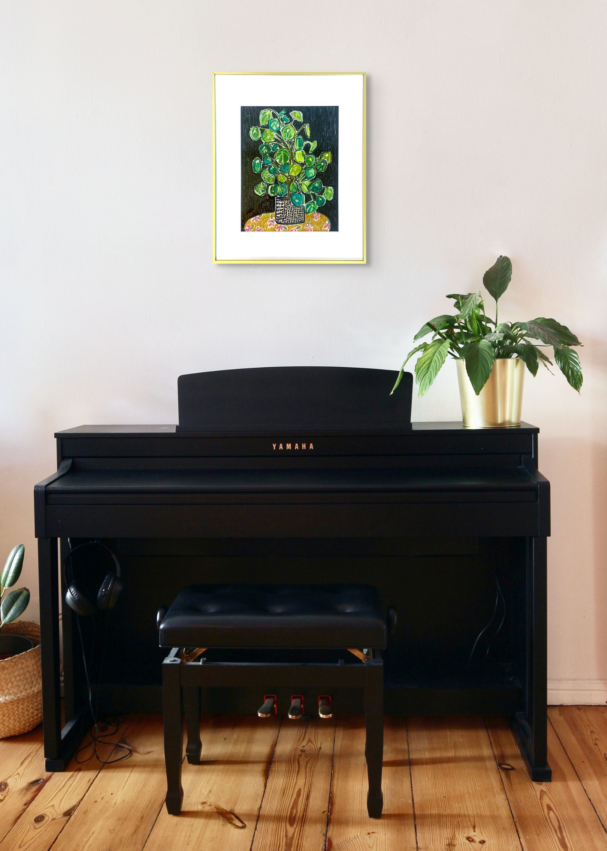 Rachel Bunteman's artwork hangs perfectly over a black upright piano with a small plant on the edge. The metal frame blends with the metal vase.