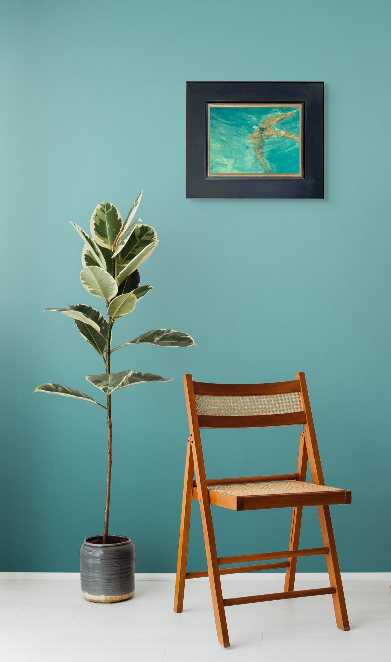 Wooden chair and potted plant against a teal wall with a Once Upon A Dream in its black frame hanging above. 
