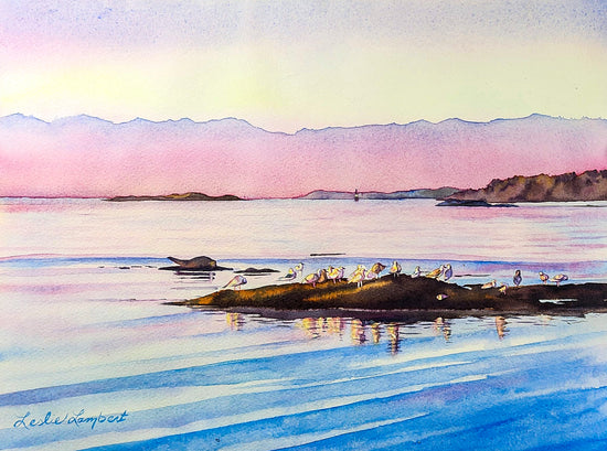 This beautiful depiction of an early morning over the water is in hues of pink of the sky and blues of the water. They blend beautifully together. A rock formation in the water is home to a gathering of gulls. 