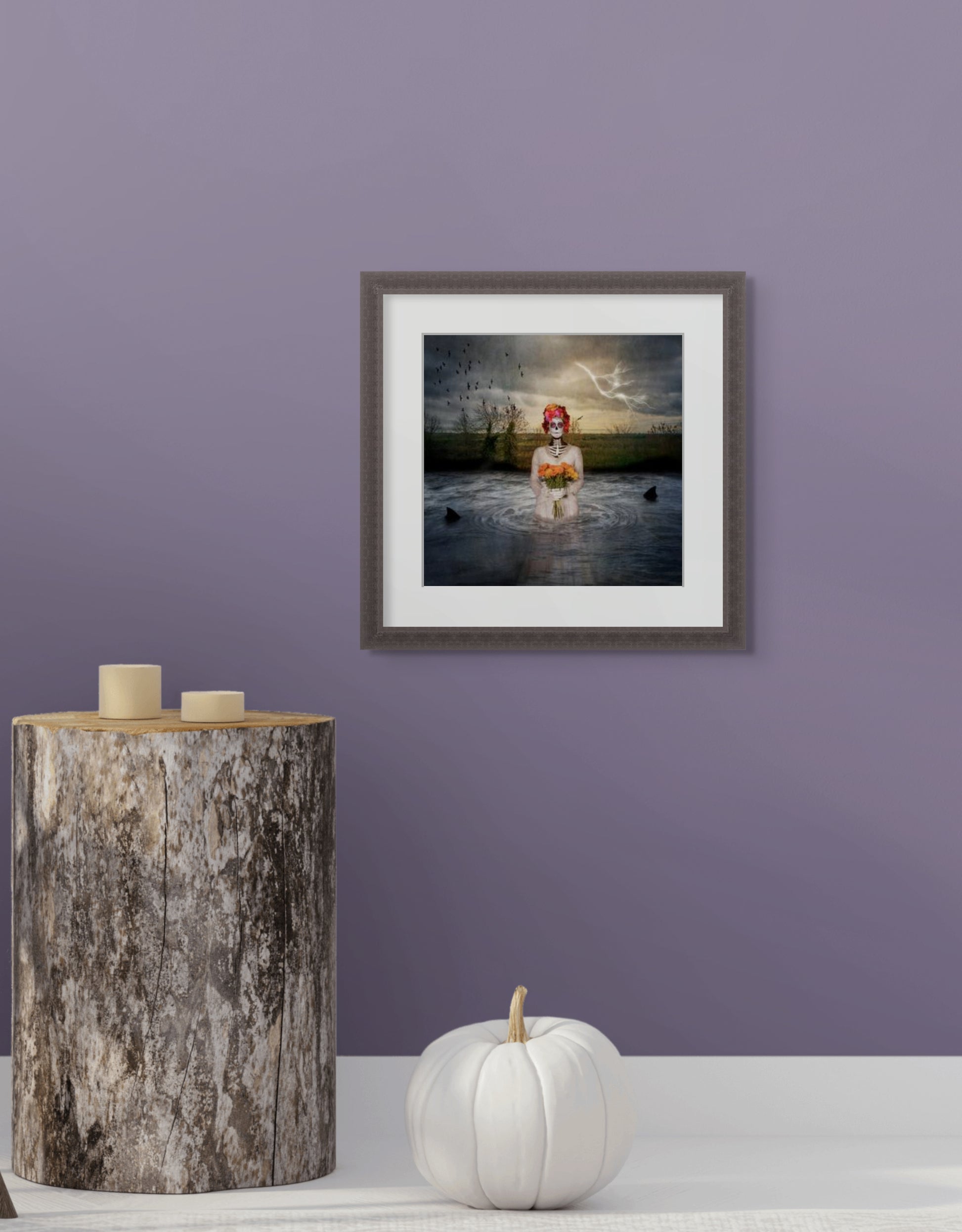 Framed image of  The Catrina on a purple wall with a wooden side table and white pumpkin.