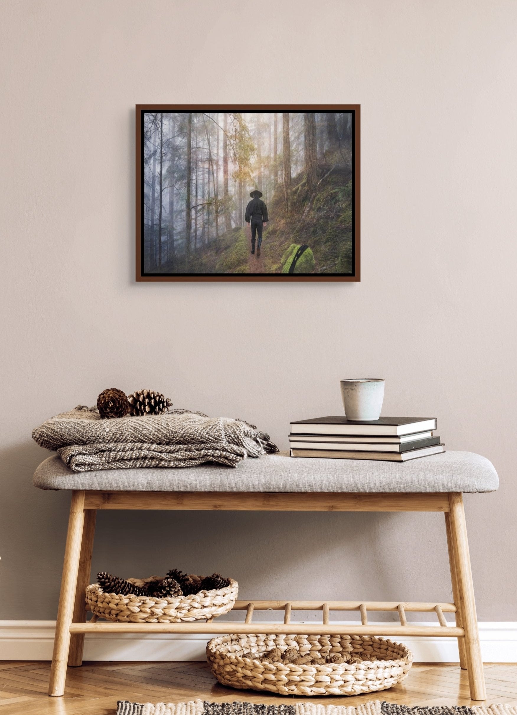 In situ image of Tired of the Masks shown here in a small brown frame with an inner black trim. The image hangs over a small cushioned table adorned with books and blankets. 