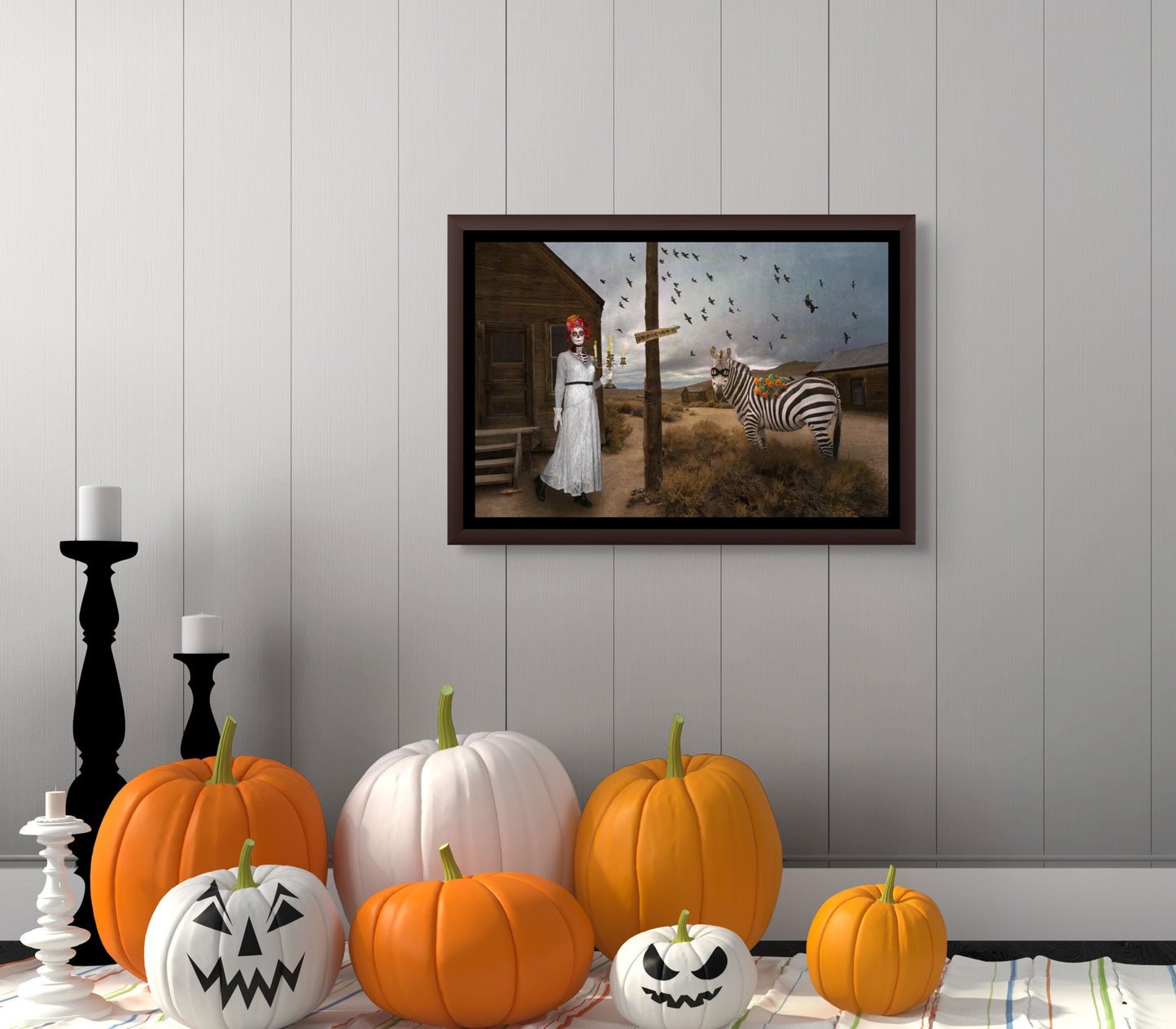 Framed image of To the Graveyard on a wall with pumpkins and candles on a table below.