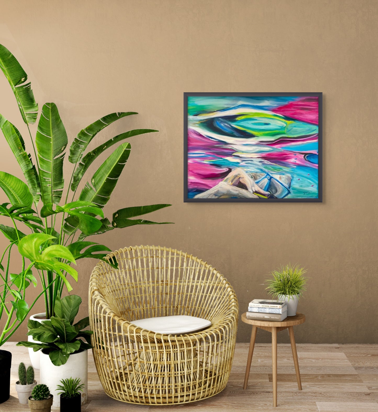 Photo shows the painting by Doris Gorin hanging on a taupe wall with a rattan chair, side table and large plant in the foreground.