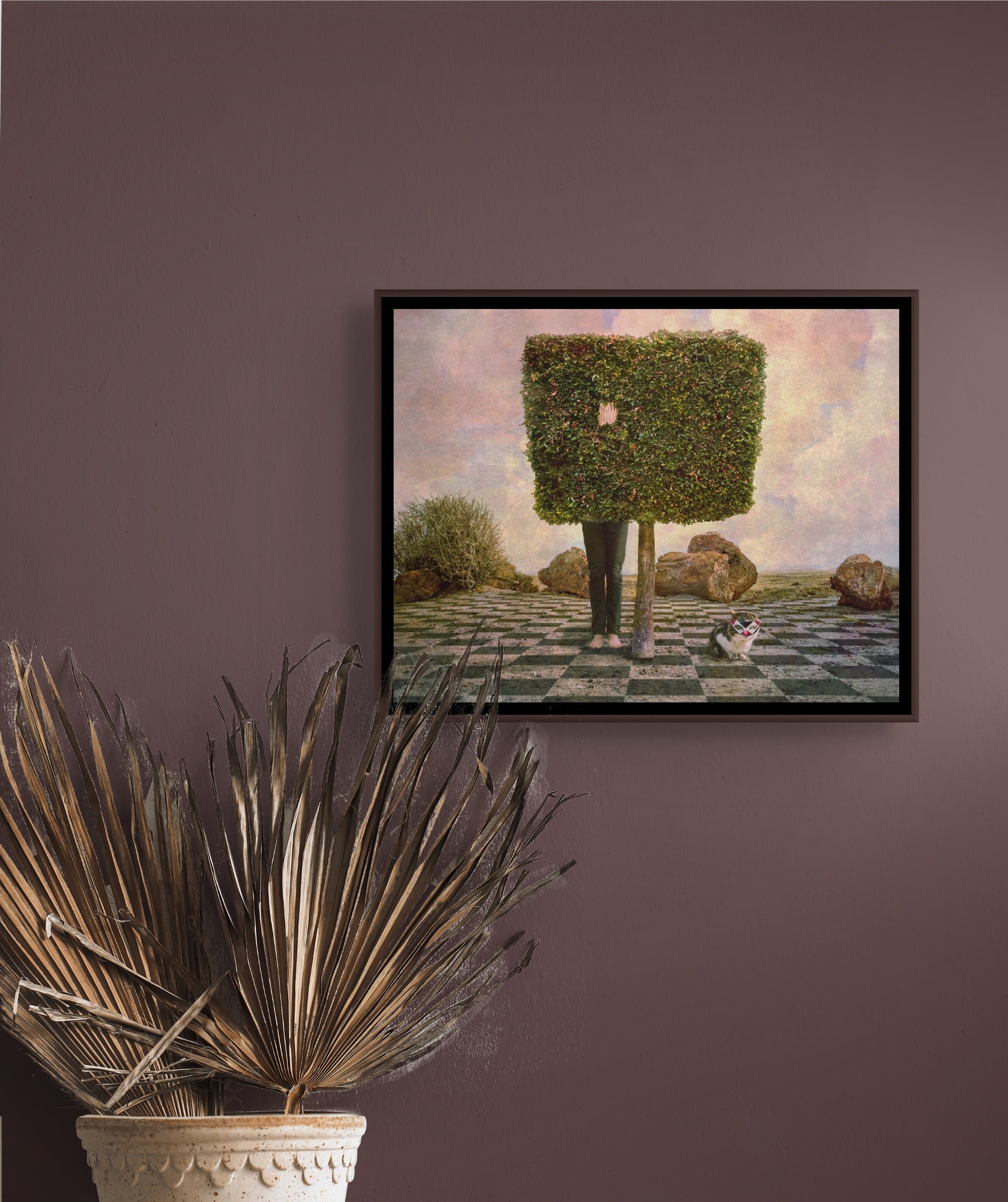 Digital composition of person hiding inside  square-shaped tree w cat in foreground wearing mask; artist Jane Ouweleen; shown in situ